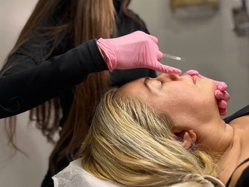 A woman receives a lip injection from a professional wearing pink gloves.