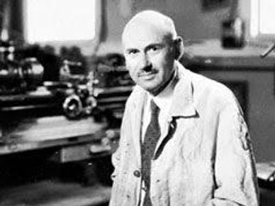 Black and white photo of a man in a lab coat in a workshop.