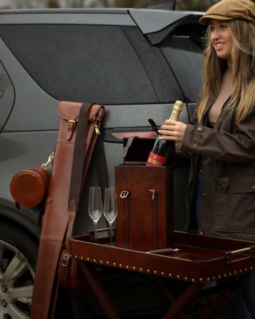 Woman opening a champagne bottle by a car with accessories.