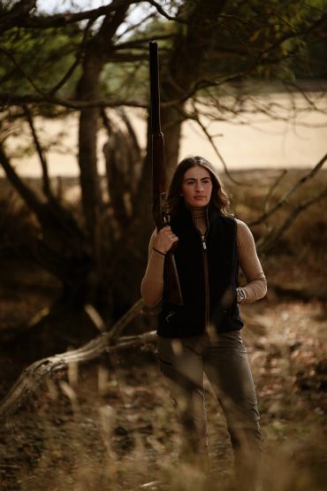 Woman holding a rifle in a forest.