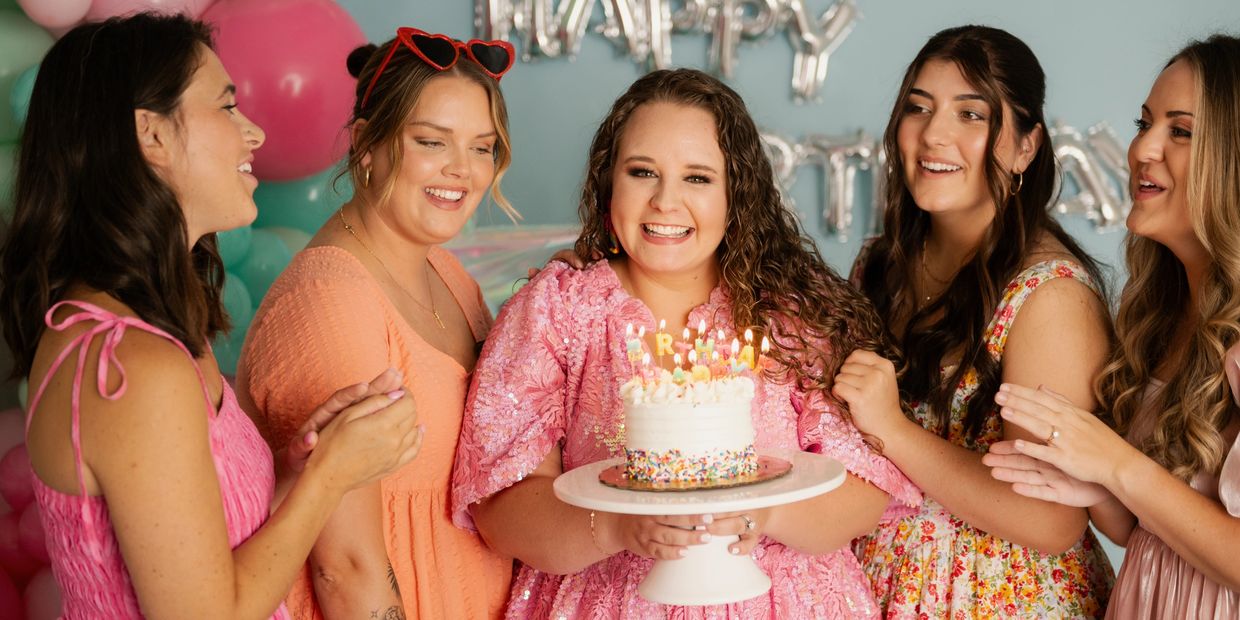 5 girls posing around birthday girl holding cake with candles and balloons behind them