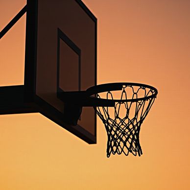 Silhouette of a basketball hoop against a warm sunset sky.