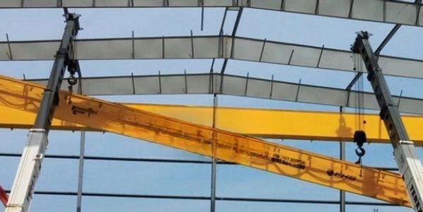 Two large yellow industrial overhead cranes inside a steel-framed building under construction.