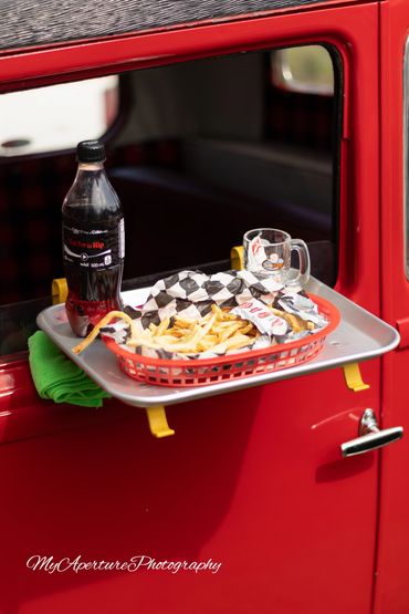 Drive-in meal on a red car window tray with fries and soda.