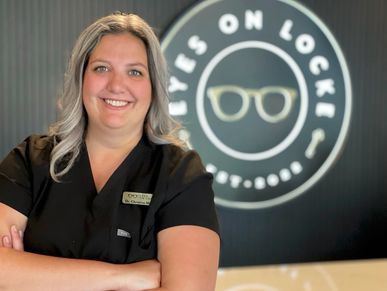 Smiling woman standing in front of an eyewear store sign.