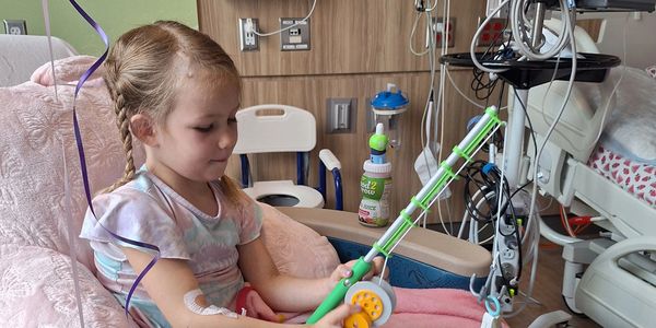 A young girl in a hospital bed plays with a fishing rod toy, smiling calmly.