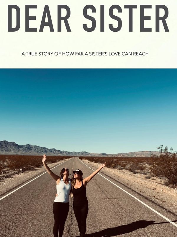 Two women on a desert road celebrating sisterly love under a clear blue sky.