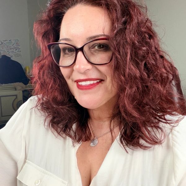 Woman with curly red hair and glasses smiling.