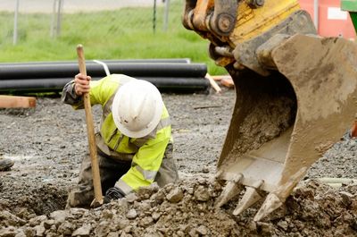 Construction worker digging near excavator bucket.