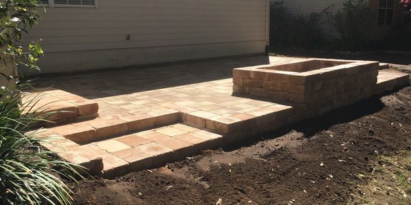 A 3-level beige patio, including a step from the house and another into the yard, plus a fire pit.