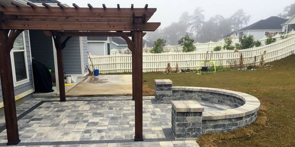A grey stone patio with a curved wall on one side and a pergola built on top.