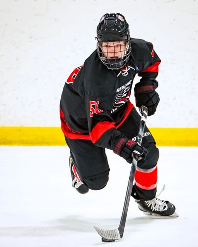 Ice hockey player in black and red uniform skating with puck.
