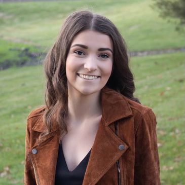 Smiling young woman outdoors in a brown jacket.