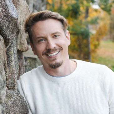 Man with light brown hair smiling by a stone wall.