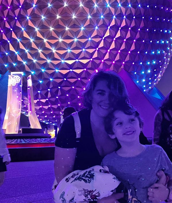 Chloe and son standing in front of the glowing globe at Epcot