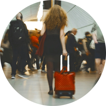 Woman with curly hair pulling a red suitcase in a busy corridor.