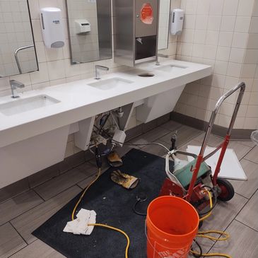 Maintenance work underway in a public restroom with tools and gloves on the floor.