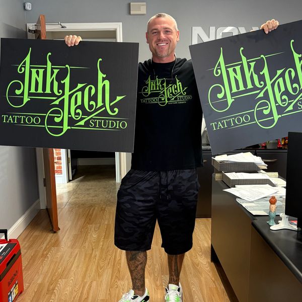 Man holding two tattoo studio signs with a matching shirt.