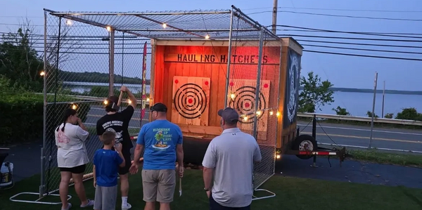 People playing axe throwing at an outdoor setup in the evening.