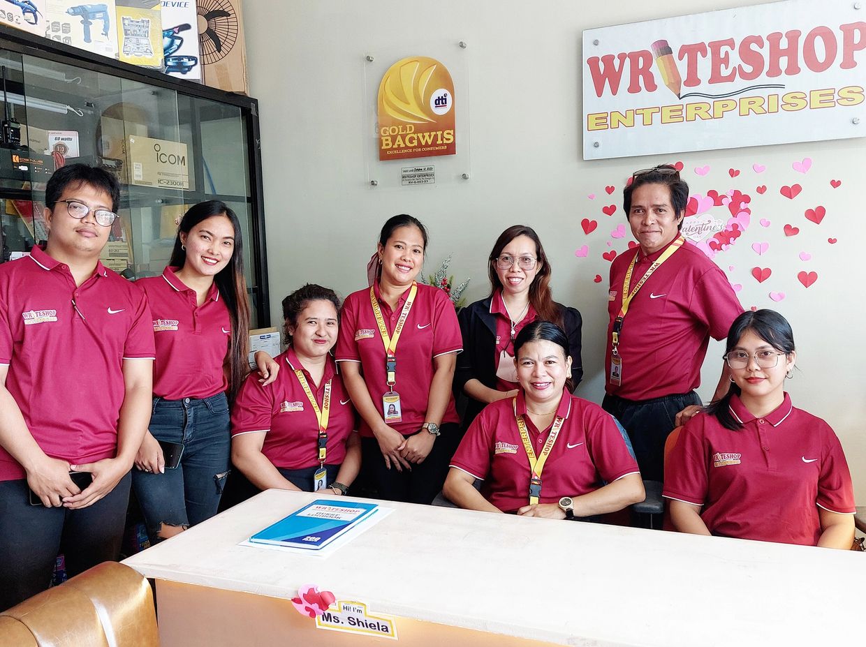 A team of eight people wearing matching maroon shirts posing in an office with a WRITESHOP sign.