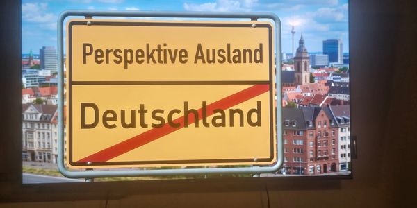 Sign indicating 'Perspective Abroad' and crossing out 'Germany' with cityscape background.