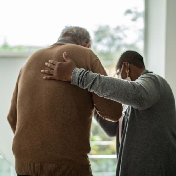 A caregiver supports an elderly man by the back.
