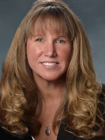 Professional portrait of a smiling woman with long curly hair and bangs.