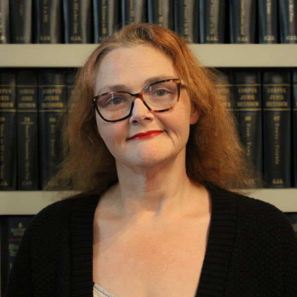 Woman with glasses and red hair standing in front of bookshelves.