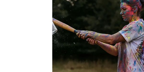 Person covered in colorful powder swinging a bat outdoors.