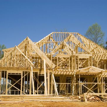 Wooden framing of a house under construction against a clear blue sky.