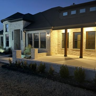 Night view of a modern house with illuminated porch and stone exterior.