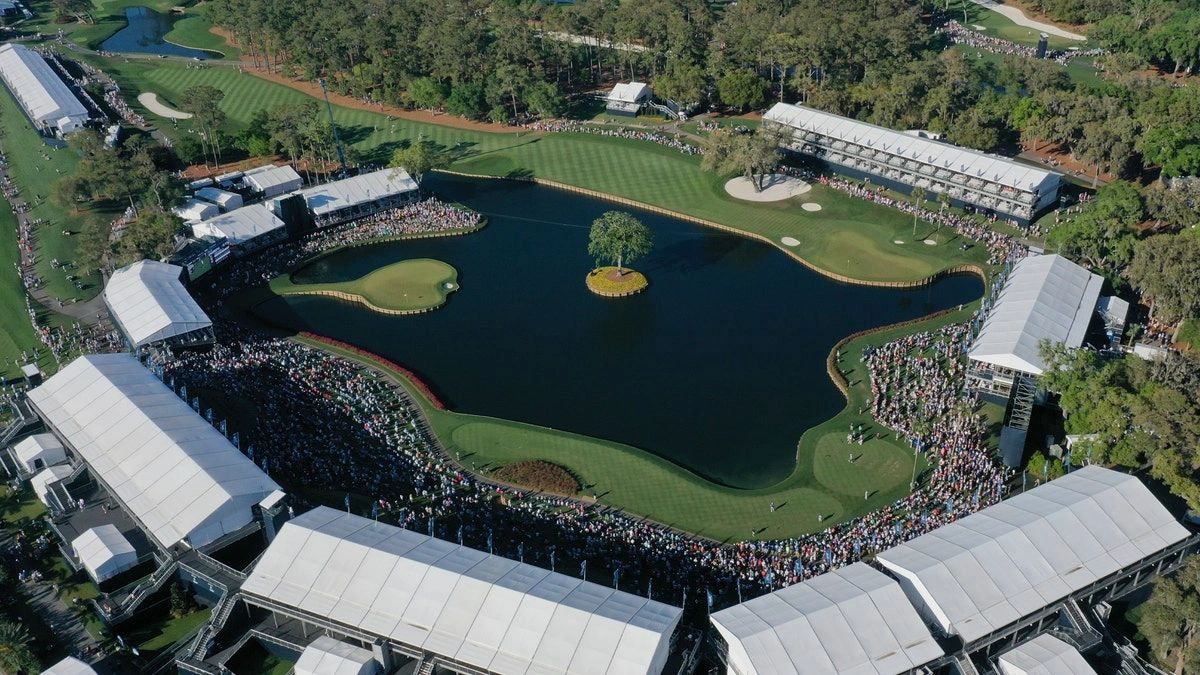 Aerial view of a golf course hole with a water hazard and spectators.