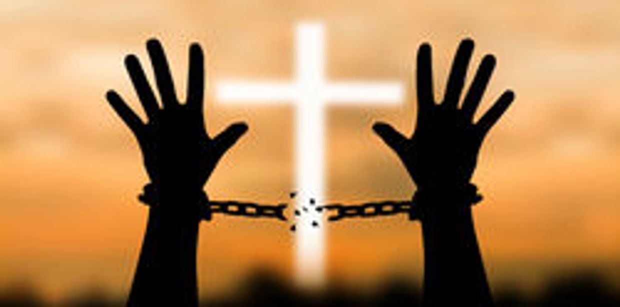 Silhouette of hands breaking chains with a cross background.