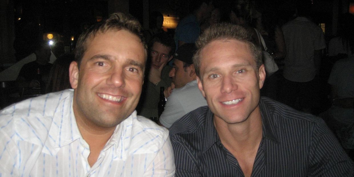 Two men smiling at a dimly lit social gathering or party.