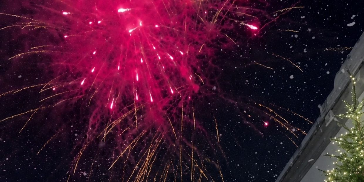 Bright pink fireworks bursting in the night sky with snow falling.