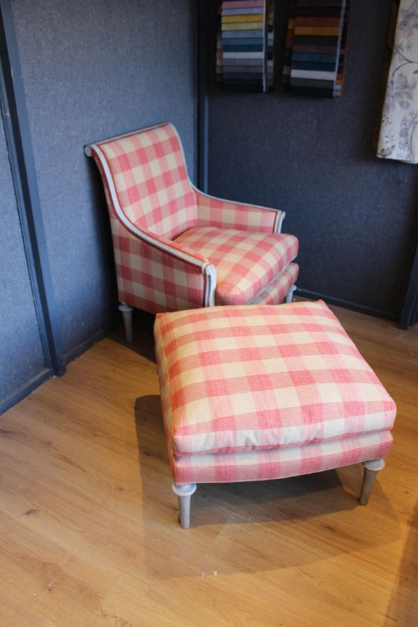 Pink and cream checkered armchair with matching ottoman on wooden floor.