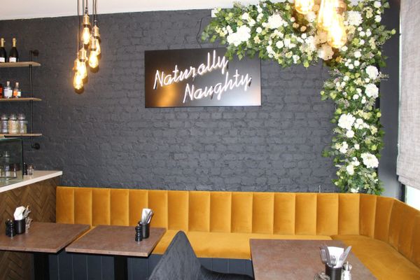 Cozy cafe corner with mustard yellow seating and floral decor under a 'Naturally Naughty' sign.