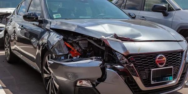 Gray sedan with front-end collision damage and broken headlight.
