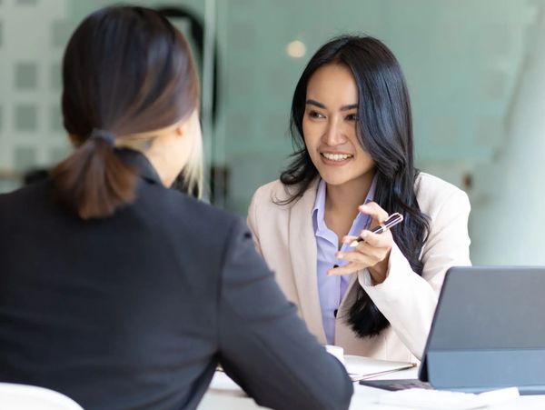 Two professional women having a conversation in an office setting.