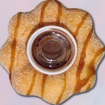 A flower-shaped pastry with caramel drizzle and a cup of coffee in the center.