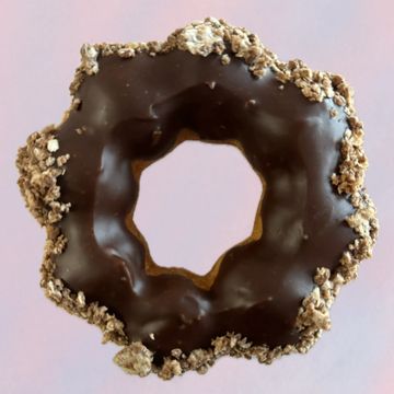 Chocolate-glazed donut with granola topping on a pink background.