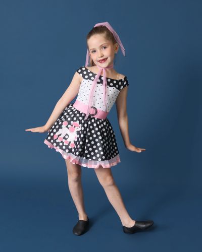 Young girl posing in a 1950s-style polka dot dress with a pink belt and headscarf.