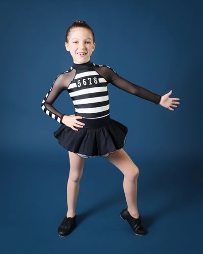 A young dancer in a black and white striped costume posing cheerfully.