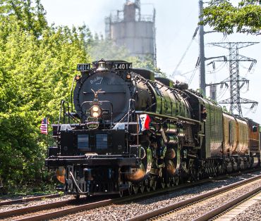 A vintage steam locomotive pulling passenger cars on a sunny day.