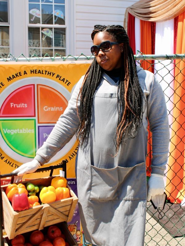 Woman with long braids holding a crate of colorful bell peppers.