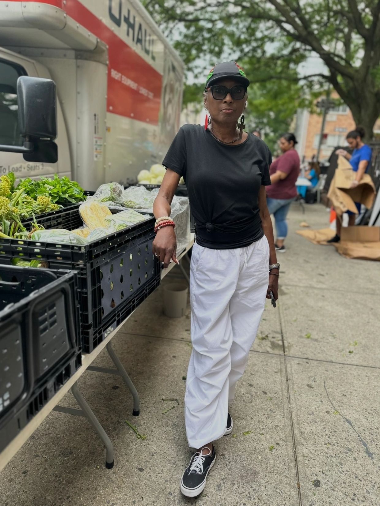 Person standing near crates of vegetables on the street.