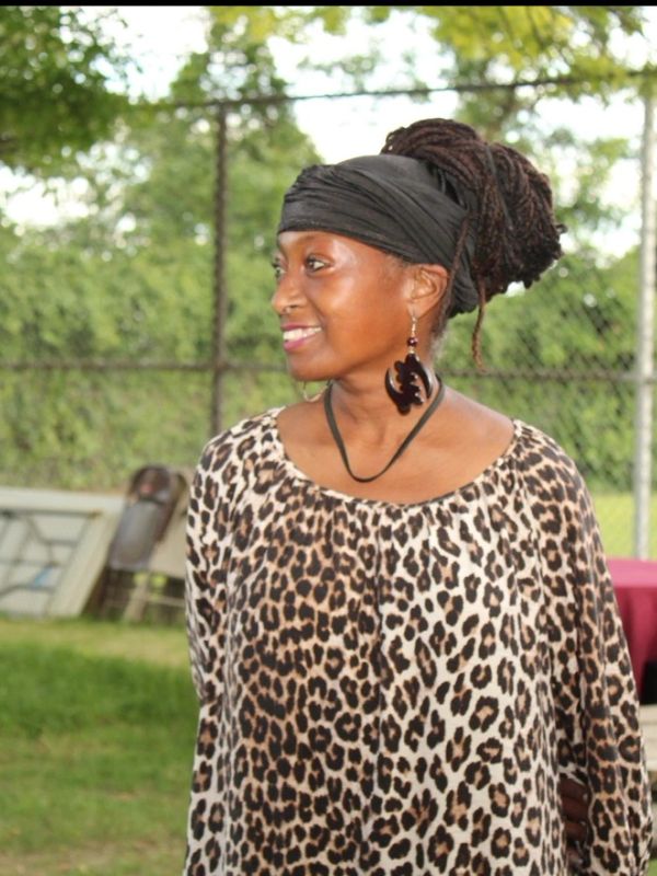 Woman smiling outdoors in a leopard print top and head wrap.