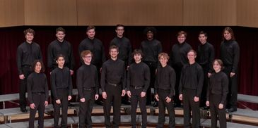 A group of young men in black outfits posing on stage risers.