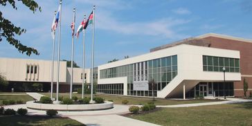 Modern academic building with flagpoles in front under a clear sky.