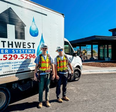 Two workers in safety gear stand beside a Northwest Water Systems truck on a sunny day.